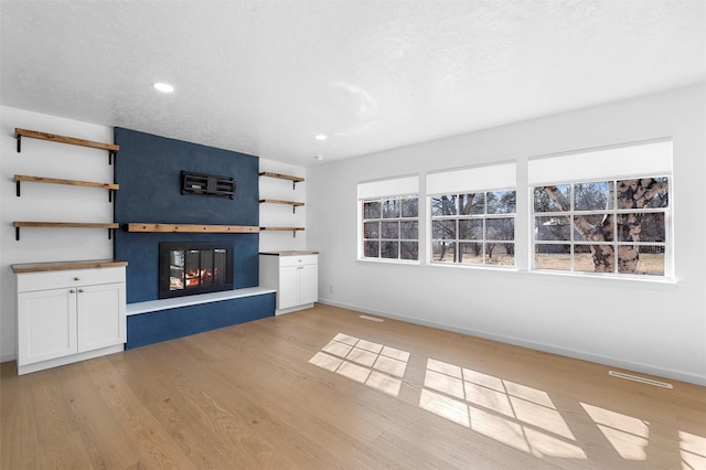 unfurnished living room featuring a glass covered fireplace, a wealth of natural light, visible vents, and light wood finished floors