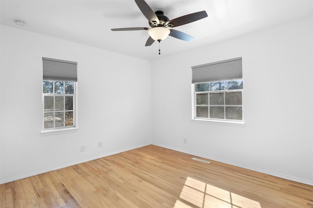 spare room with a ceiling fan, wood finished floors, visible vents, and baseboards