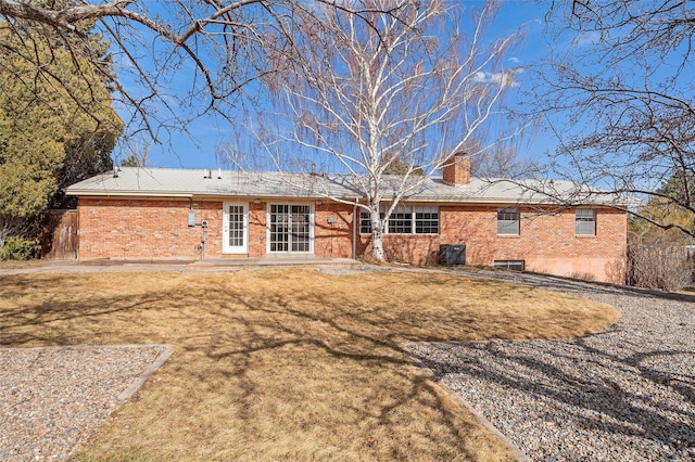 rear view of house featuring a yard, central air condition unit, brick siding, and a chimney