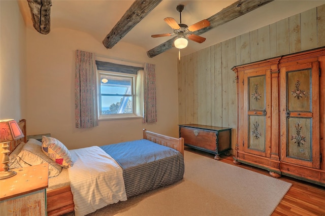 bedroom featuring a ceiling fan, beam ceiling, wood finished floors, and wood walls