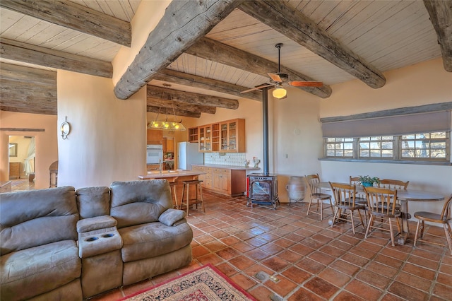 living room featuring dark tile patterned floors, wood ceiling, a wood stove, and a ceiling fan