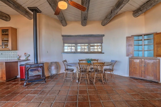 tiled dining room featuring wooden ceiling, a wood stove, a ceiling fan, and beam ceiling