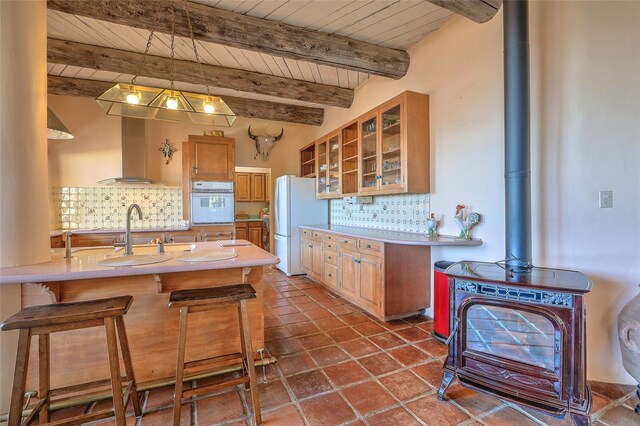 kitchen featuring backsplash, light countertops, a kitchen breakfast bar, white appliances, and wall chimney exhaust hood