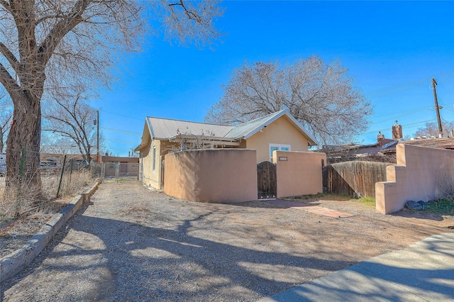 view of home's exterior featuring stucco siding, a gate, fence, and metal roof