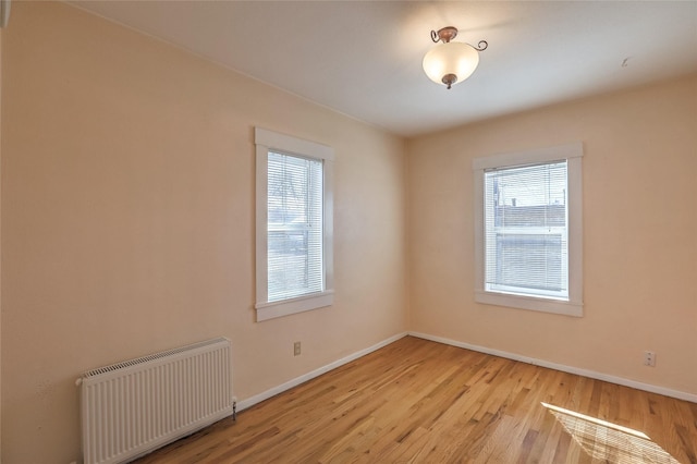 empty room featuring light wood-style flooring, radiator, and baseboards