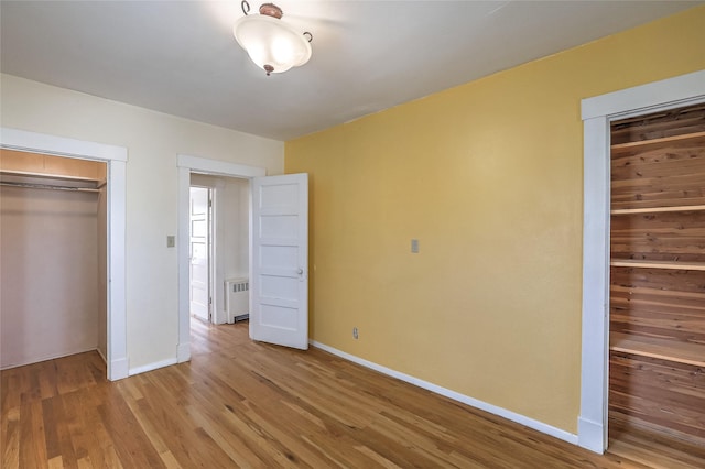 unfurnished bedroom with a closet, radiator, baseboards, and light wood finished floors