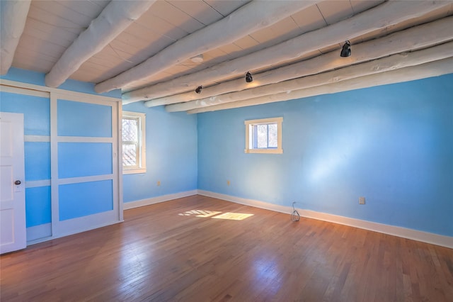 empty room featuring baseboards, beam ceiling, wood ceiling, and wood finished floors