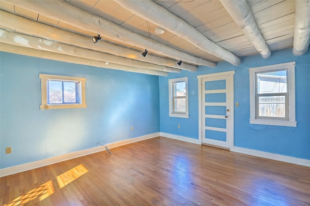 empty room with beam ceiling, wood finished floors, and baseboards