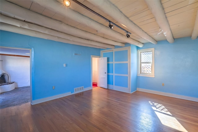 spare room with wood finished floors, a wood stove, beamed ceiling, and visible vents