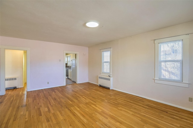 unfurnished room featuring light wood-style flooring, radiator heating unit, and baseboards