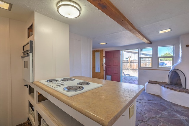 kitchen with light countertops, beam ceiling, stone finish floor, white appliances, and a textured ceiling