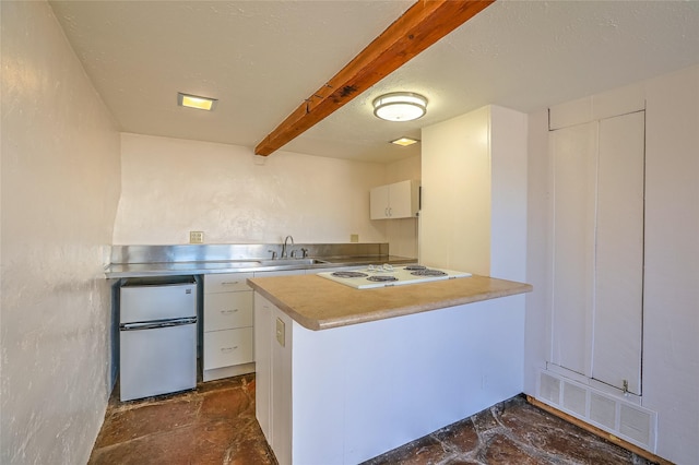 kitchen featuring visible vents, stainless steel counters, a peninsula, freestanding refrigerator, and white electric stovetop