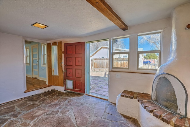 doorway to outside with stone flooring, beamed ceiling, and a textured ceiling