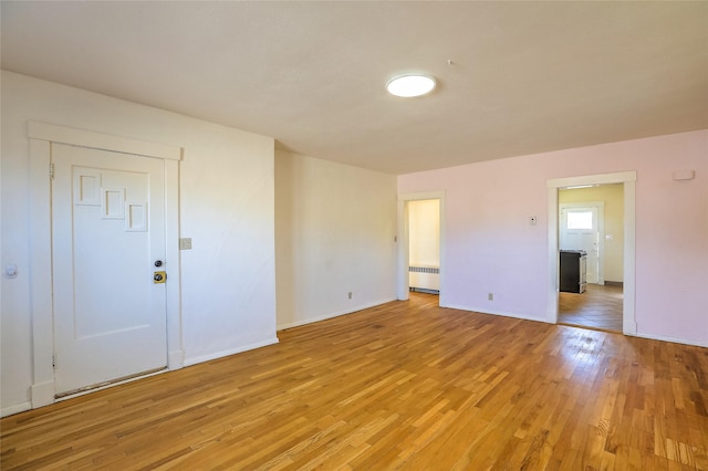 spare room with baseboards, radiator heating unit, and light wood finished floors