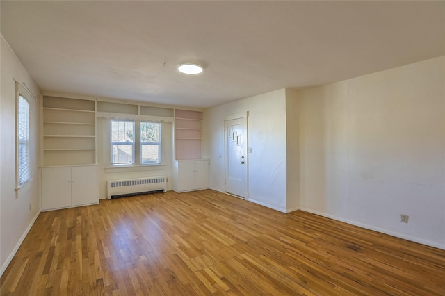 unfurnished room with built in shelves, radiator, baseboards, and wood-type flooring