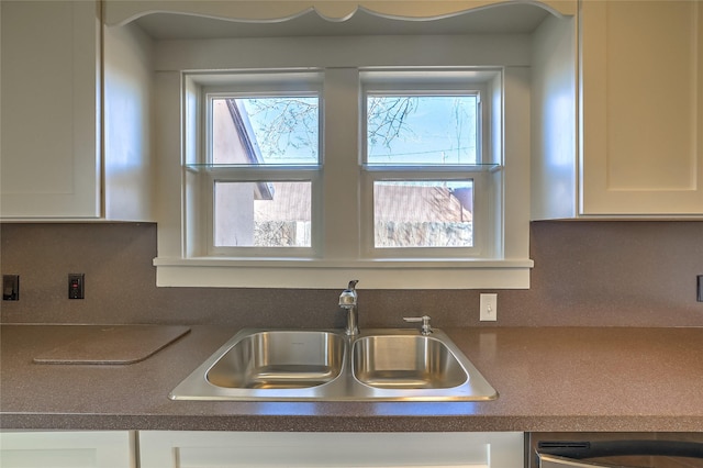 kitchen featuring a sink, backsplash, dark countertops, and white cabinetry