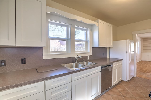 kitchen with light tile patterned floors, a sink, white cabinets, dishwasher, and dark countertops