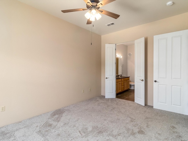 unfurnished bedroom with a ceiling fan, visible vents, dark carpet, and connected bathroom