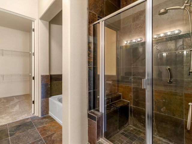 bathroom with a spacious closet, a stall shower, a garden tub, and stone tile flooring