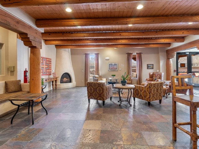 living area featuring beam ceiling, a large fireplace, wood ceiling, and stone tile floors