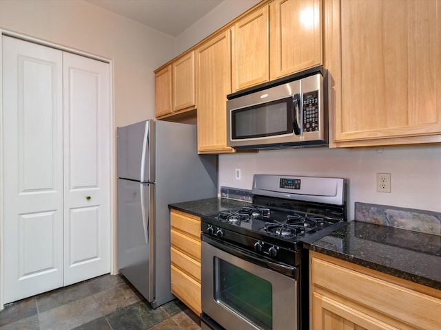 kitchen featuring light brown cabinets, stainless steel appliances, stone finish flooring, and dark stone counters