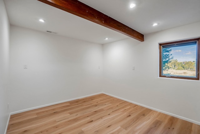 empty room with beam ceiling, visible vents, light wood-type flooring, and baseboards