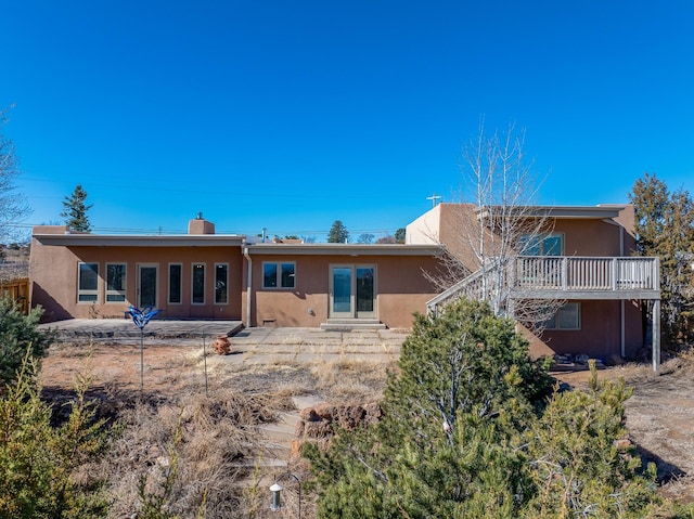 back of property with stairway, stucco siding, a chimney, a deck, and a patio