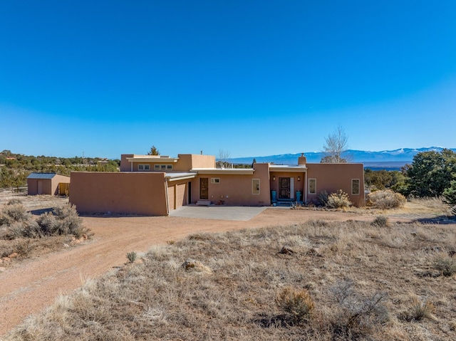 back of property featuring a mountain view, stucco siding, an attached garage, and dirt driveway