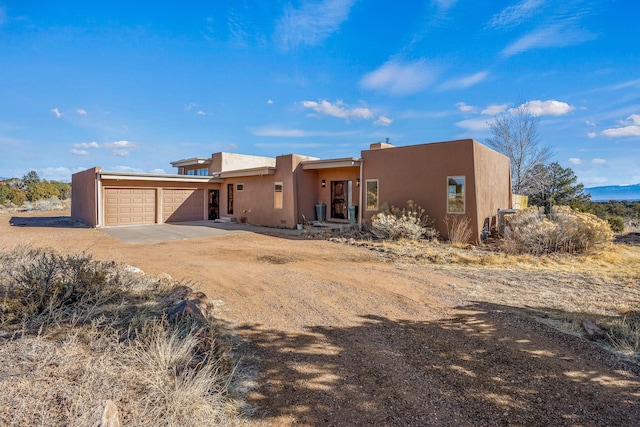 pueblo-style home featuring an attached garage, driveway, and stucco siding