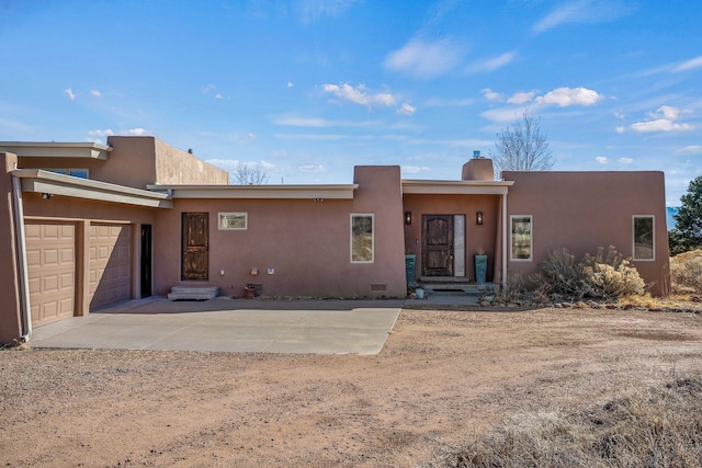 pueblo-style house featuring stucco siding, driveway, a chimney, and a garage