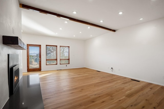 unfurnished living room featuring beam ceiling, light wood-style flooring, a warm lit fireplace, recessed lighting, and baseboards