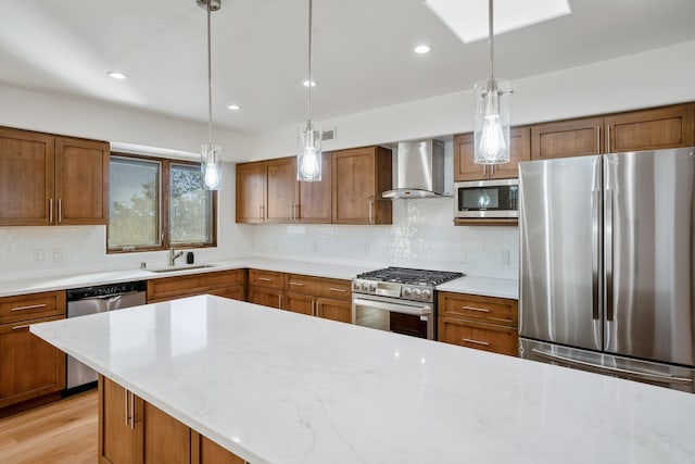 kitchen featuring decorative light fixtures, decorative backsplash, brown cabinets, appliances with stainless steel finishes, and wall chimney exhaust hood