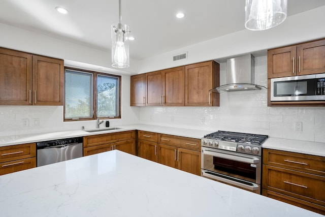 kitchen with a sink, decorative backsplash, appliances with stainless steel finishes, pendant lighting, and wall chimney exhaust hood