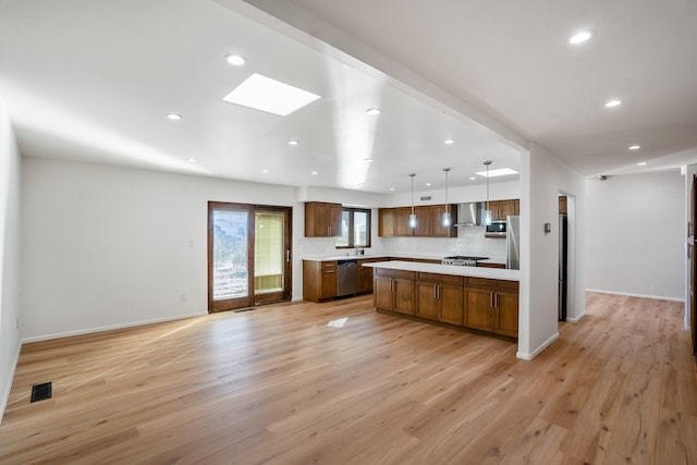 kitchen featuring open floor plan, appliances with stainless steel finishes, light countertops, and wall chimney exhaust hood