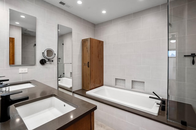 bathroom featuring tile walls, a garden tub, visible vents, and a sink