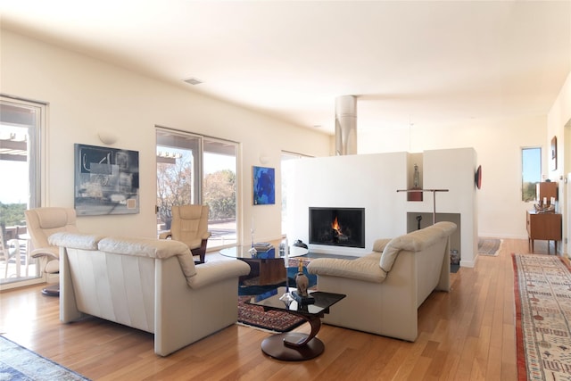 living room with visible vents, a lit fireplace, and light wood finished floors