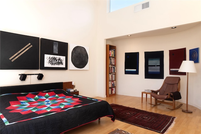 bedroom with visible vents, a high ceiling, and wood finished floors