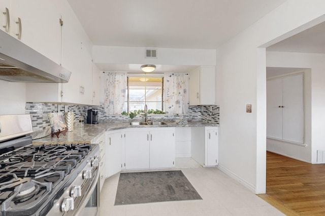 kitchen featuring visible vents, a sink, under cabinet range hood, white cabinetry, and stainless steel gas range