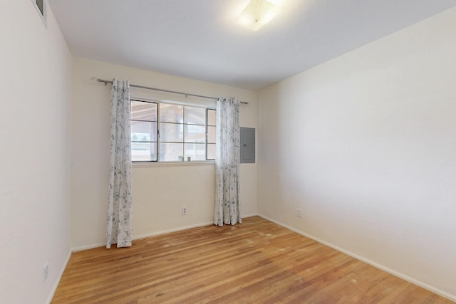 empty room featuring light wood-style flooring, electric panel, and baseboards