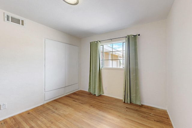 spare room with light wood-type flooring, visible vents, and baseboards