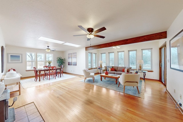 living room featuring light wood-style floors, baseboards, a ceiling fan, and a skylight