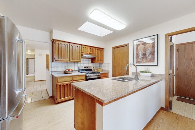 kitchen featuring a sink, appliances with stainless steel finishes, a peninsula, under cabinet range hood, and a skylight