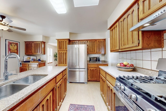 kitchen with tasteful backsplash, a sink, appliances with stainless steel finishes, light wood-style floors, and under cabinet range hood