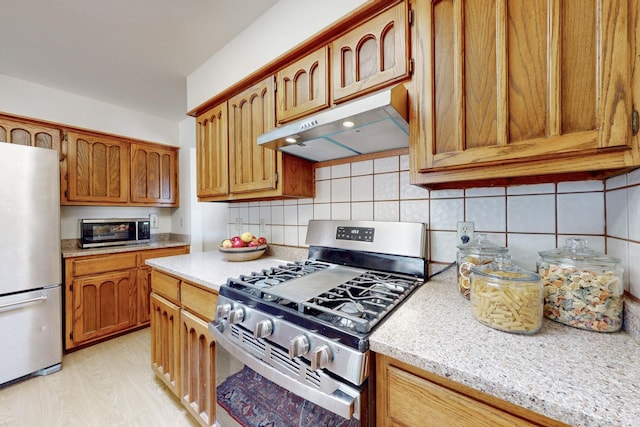 kitchen featuring under cabinet range hood, light wood-type flooring, decorative backsplash, and appliances with stainless steel finishes