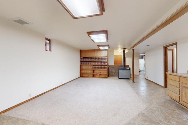 finished basement with a wood stove, baseboards, and visible vents