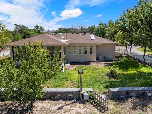 back of property with a yard, a shingled roof, fence, and central AC