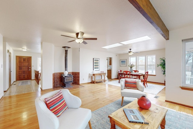living room featuring a skylight, a wood stove, ceiling fan, and light wood-style floors