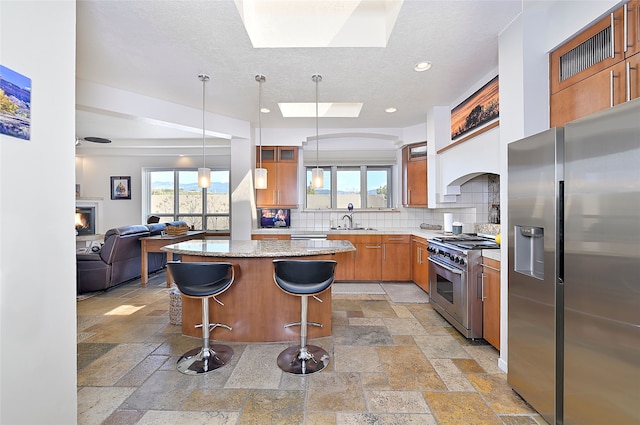 570 Via Arista, Santa Fe, NM 87506 - kitchen featuring stone tile floors, open floor plan, appliances with stainless steel finishes, brown cabinetry, and decorative backsplash