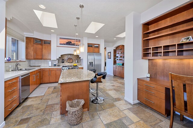570 Via Arista, Santa Fe, NM 87506 - kitchen with a sink, stone tile flooring, appliances with stainless steel finishes, a breakfast bar area, and a skylight