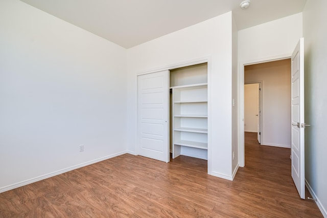unfurnished bedroom featuring baseboards, wood finished floors, and a closet